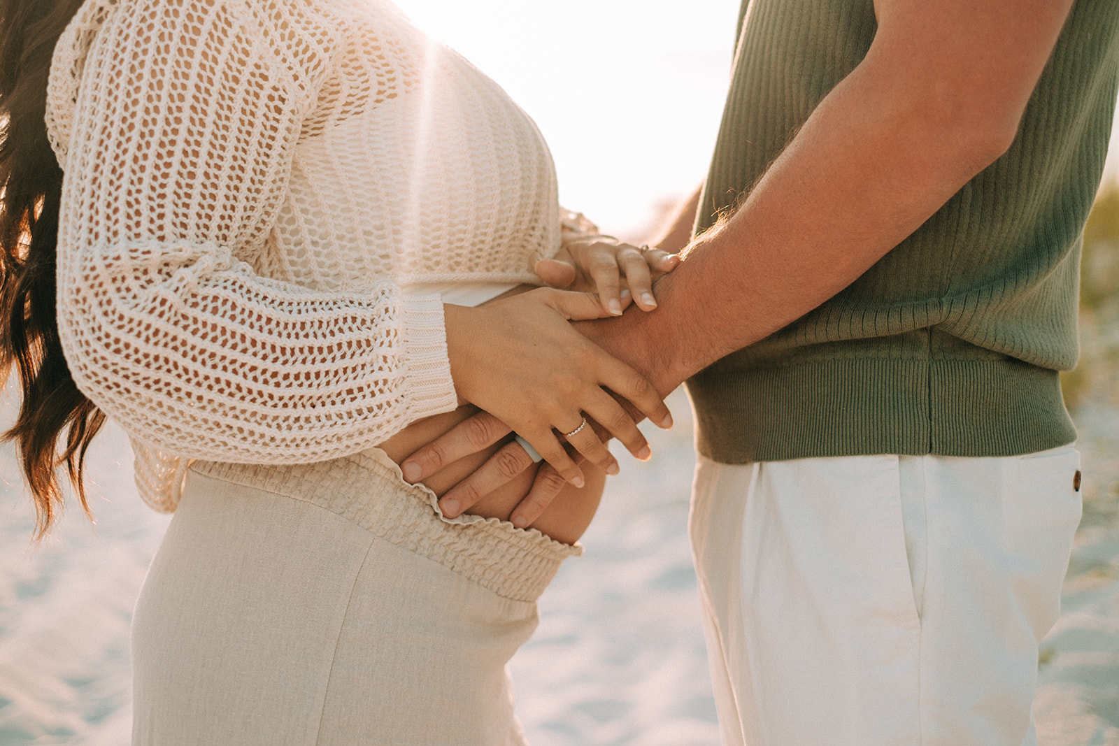 A couple holding hands gently over a baby bump in warm light